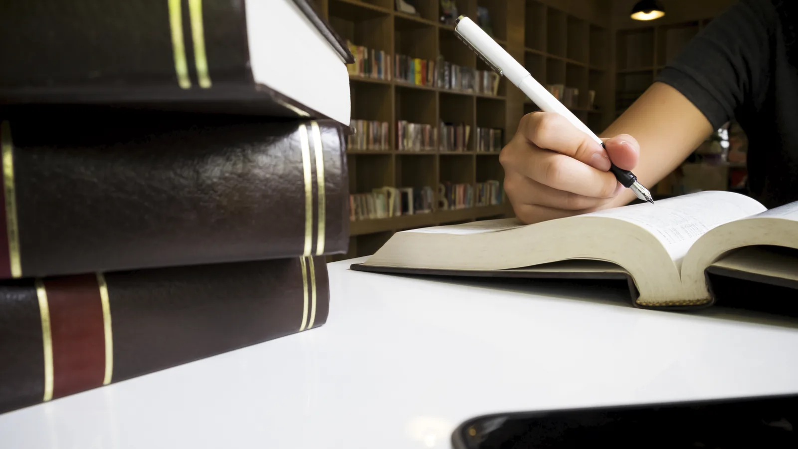 A person takes notes beside stacked law books in a library.
