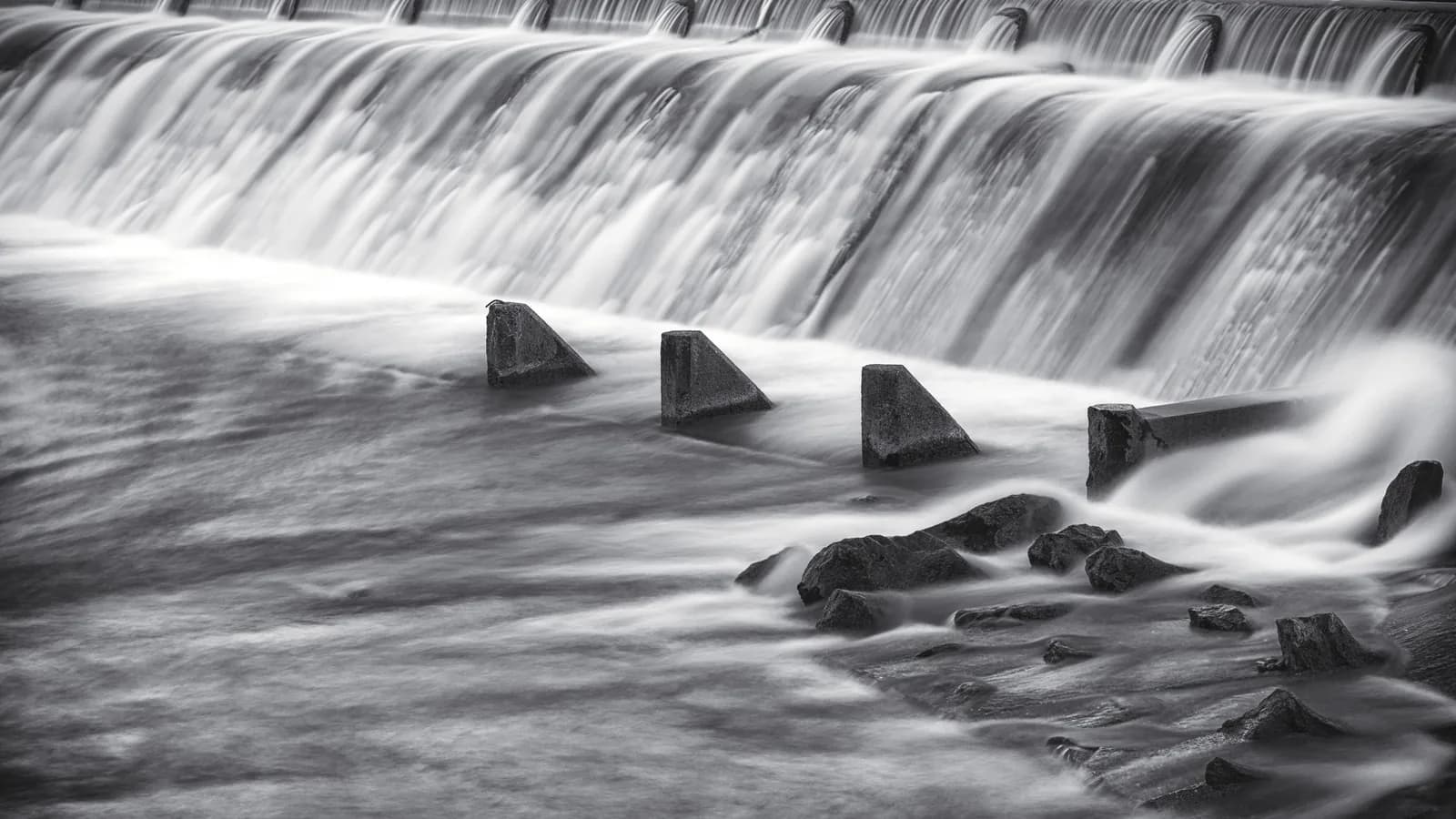 Black-and-white long exposure of water pouring over a river dam.