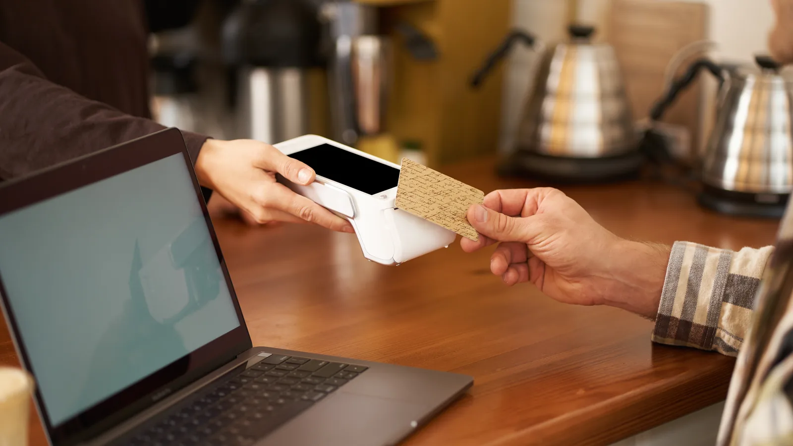 A customer taps a phone to pay at a cafe counter next to a laptop.