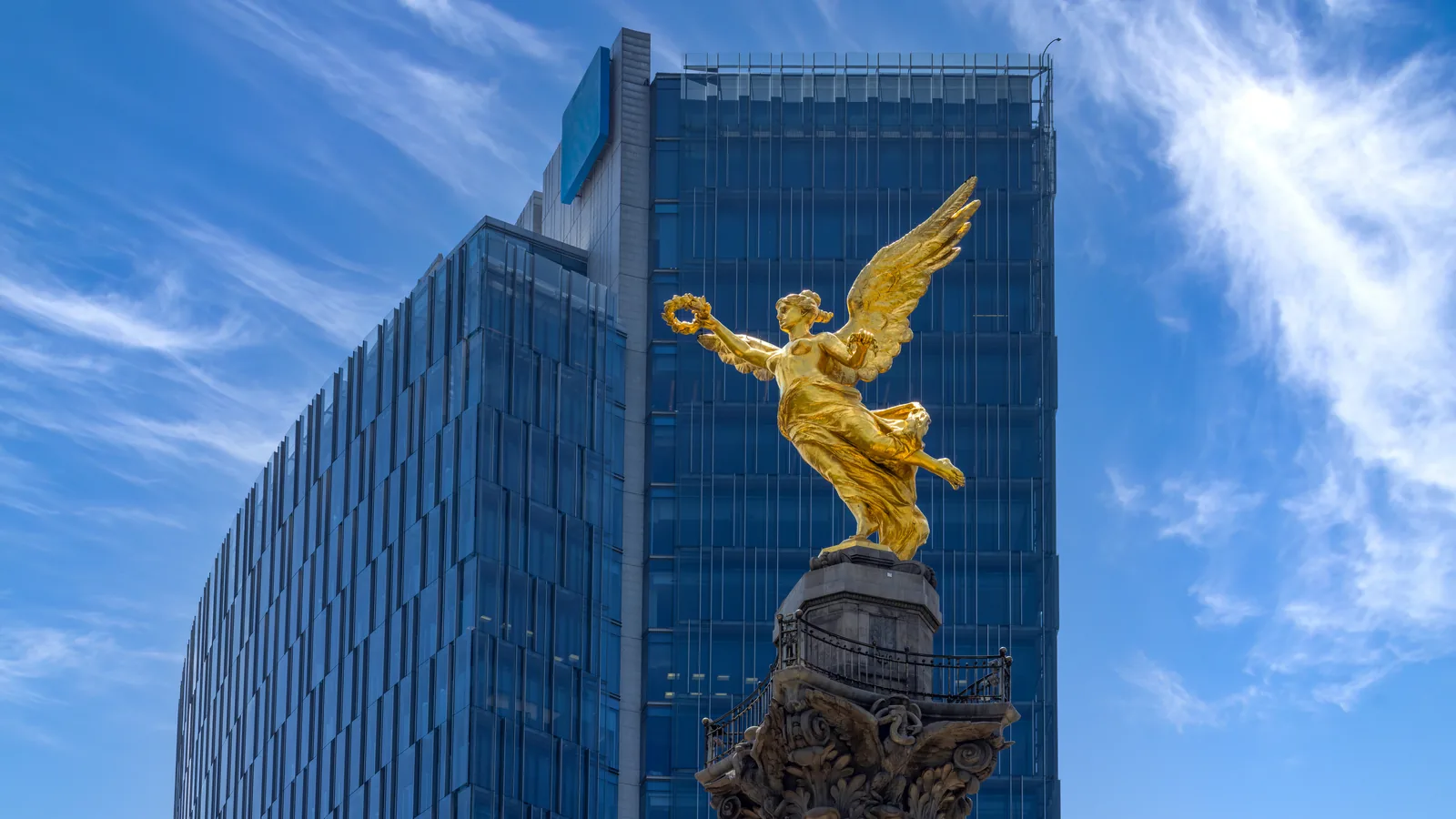 The golden Angel of Independence statue in Mexico City in front of a glass office tower.