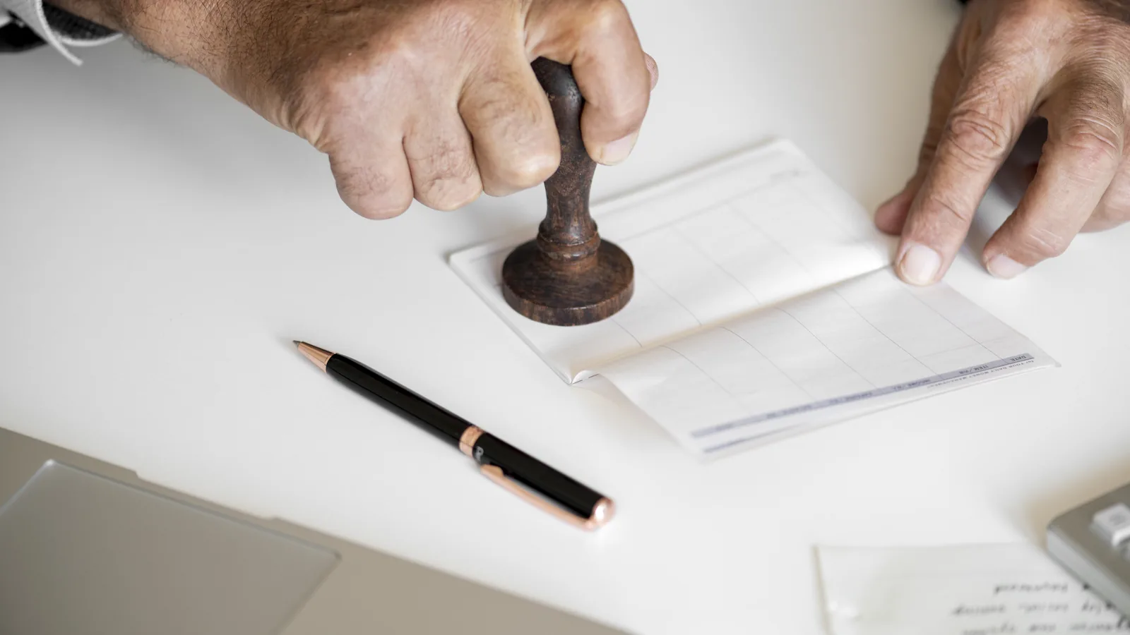 Hands pressing a rubber stamp onto paperwork on a white desk.