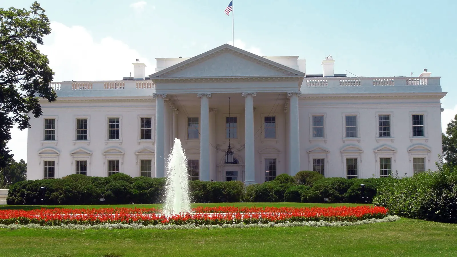 The north facade of the White House with a fountain and red flower beds.