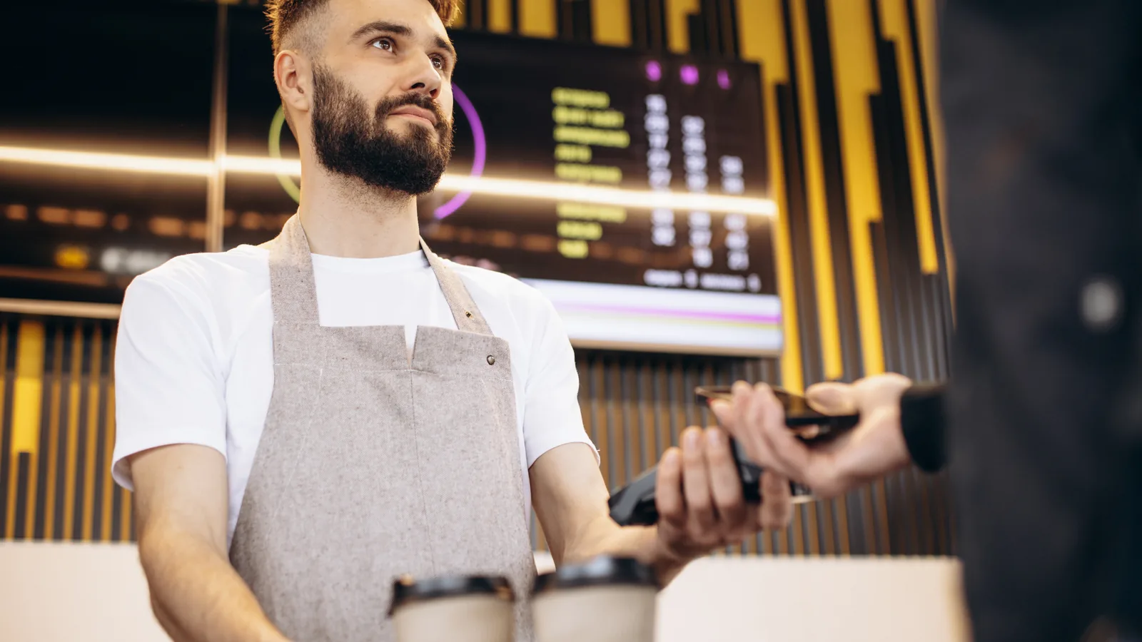 A cafe worker holds a card terminal while a customer pays.