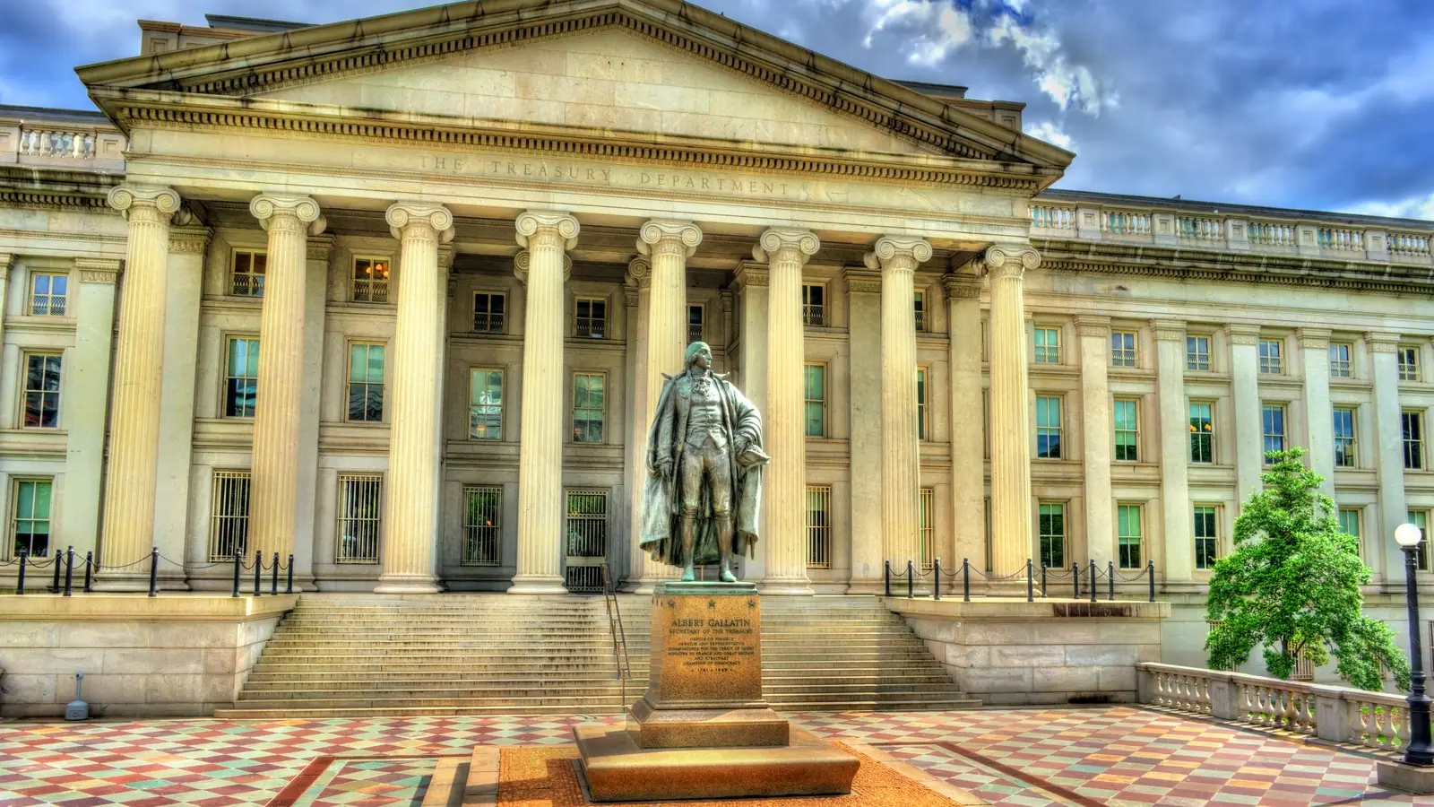 The columned stone facade of the U.S. Treasury Department building in Washington, with the Albert Gallatin statue in front.
